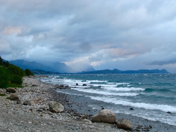 A moody sky and rocky beach with mountains in the background