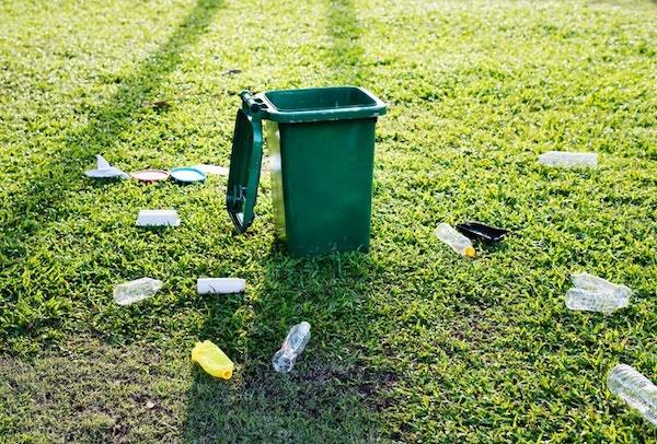 plastic bottles on a green lawn by a garbage can - this is why reusable products need to exist