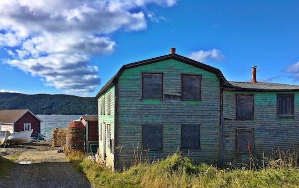 Conche Newfoundland boarded up green wood building with fishing pots and boat in the background