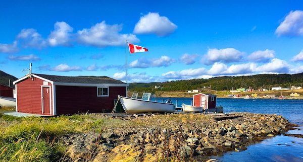 Visit Newfoundland Canada with red wooden building Canadian flag and boat shore