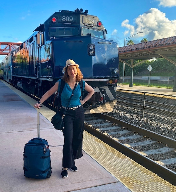 Nora Dunn, The Professional Hobo, with rolling luggage in front of a train