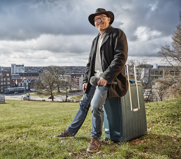 The Radio Vagabond sitting on luggage with a microphone 